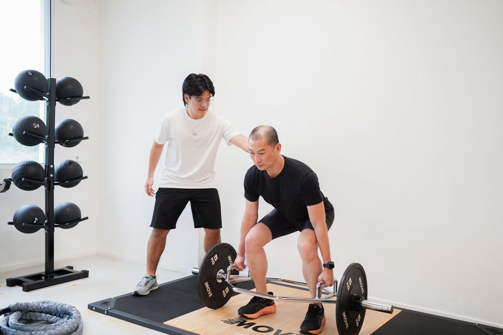 A coach guiding an older client through a trap bar lift