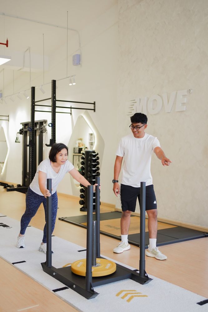 A coach guiding a client as she pushes a weighted sled