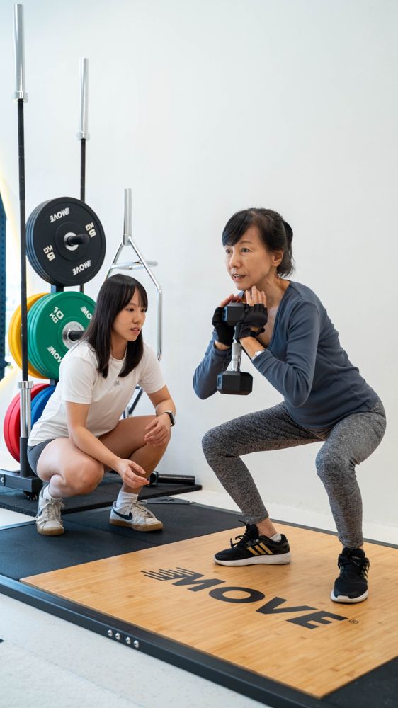 A coach guiding an older client through a goblet squat
